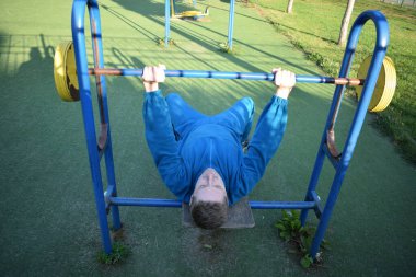 A dedicated young athlete puts in the hard work, vigorously training on gym equipment outdoors to prepare his body. He builds strength and endurance before hitting the field or court for competition