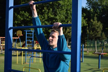 A dedicated young athlete puts in the hard work, vigorously training on gym equipment outdoors to prepare his body. He builds strength and endurance before hitting the field or court for competition