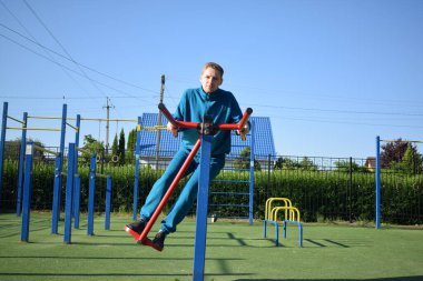 A dedicated young athlete puts in the hard work, vigorously training on gym equipment outdoors to prepare his body. He builds strength and endurance before hitting the field or court for competition