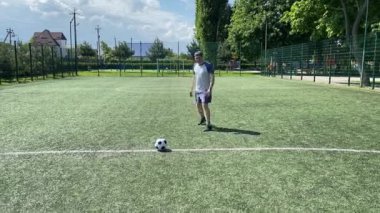 Spor giyimli genç bir adam sabah futbol sahasında antrenman yapıyor. Spor için adanmışlık ve tutku, sabah egzersizinin özü ve açık havada pratik.