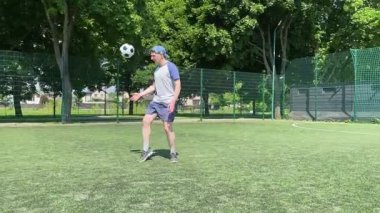 Spor giyimli genç bir adam sabah futbol sahasında antrenman yapıyor. Spor için adanmışlık ve tutku, sabah egzersizinin özü ve açık havada pratik.
