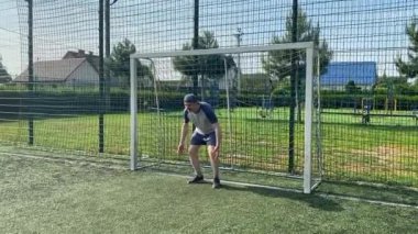 Spor giyimli genç bir adam sabah futbol sahasında antrenman yapıyor. Spor için adanmışlık ve tutku, sabah egzersizinin özü ve açık havada pratik.