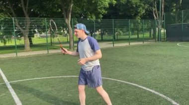 Spor giyim sektöründe genç bir adam sabah bir spor sahasında badminton oynuyor. Spor için adanmışlık ve tutku, sabah egzersizinin özü ve açık havada pratik.