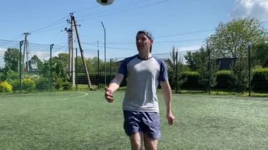 Spor giyimli genç bir adam sabah futbol sahasında antrenman yapıyor. Spor için adanmışlık ve tutku, sabah egzersizinin özü ve açık havada pratik.