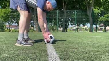 Spor giyimli genç bir adam sabah futbol sahasında antrenman yapıyor. Spor için adanmışlık ve tutku, sabah egzersizinin özü ve açık havada pratik.