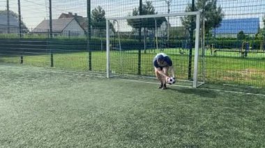 Spor giyimli genç bir adam sabah futbol sahasında antrenman yapıyor. Spor için adanmışlık ve tutku, sabah egzersizinin özü ve açık havada pratik.