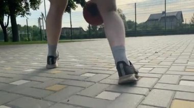 Alçak mevkide spor giyim sektöründe genç bir adam basketbol oynuyor, sabah spor salonunda antrenman yapıyor. Spor için adanmışlık ve tutku, sabah egzersizinin özü ve açık havada pratik.