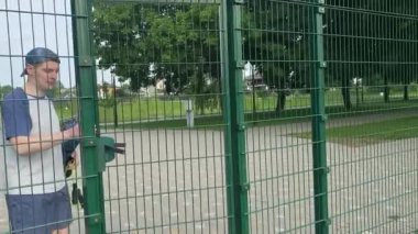 Spor giyimli genç bir adam antrenmana hazırlanıyor, sabahları spor sahasında fiziksel egzersiz için spor aletleri taşıyor. Forma olan bağlılığı odaklanma ve enerjiyle eğitim rutinini gerçekleştiriyor.