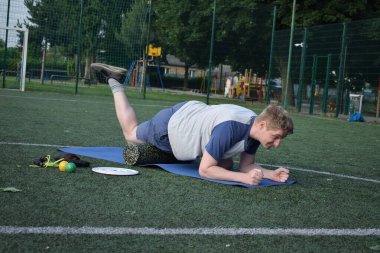 Spor giyim sektöründe genç bir adam sabah spor sahasında spor aleti kullanarak spor yapıyor. Forma olan bağlılığı odaklanma ve enerjiyle eğitim rutinini gerçekleştiriyor.