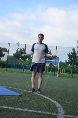 Spor giyim sektöründe genç bir adam sabah spor sahasında spor aleti kullanarak spor yapıyor. Forma olan bağlılığı odaklanma ve enerjiyle eğitim rutinini gerçekleştiriyor.