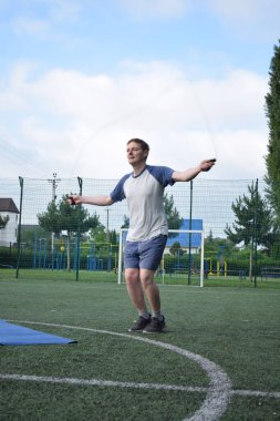 Spor giyim sektöründe genç bir adam sabah spor sahasında spor aleti kullanarak spor yapıyor. Forma olan bağlılığı odaklanma ve enerjiyle eğitim rutinini gerçekleştiriyor.