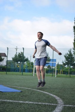 Spor giyim sektöründe genç bir adam sabah spor sahasında spor aleti kullanarak spor yapıyor. Forma olan bağlılığı odaklanma ve enerjiyle eğitim rutinini gerçekleştiriyor.