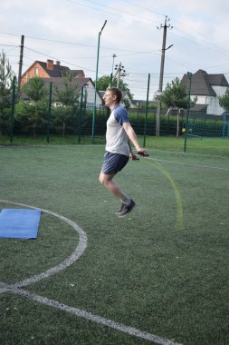 Spor giyim sektöründe genç bir adam sabah spor sahasında spor aleti kullanarak spor yapıyor. Forma olan bağlılığı odaklanma ve enerjiyle eğitim rutinini gerçekleştiriyor.