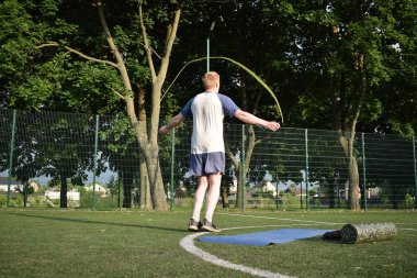 Spor giyim sektöründe genç bir adam sabah spor sahasında spor aleti kullanarak spor yapıyor. Forma olan bağlılığı odaklanma ve enerjiyle eğitim rutinini gerçekleştiriyor.