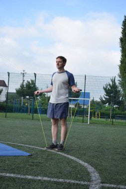 Spor giyim sektöründe genç bir adam sabah spor sahasında spor aleti kullanarak spor yapıyor. Forma olan bağlılığı odaklanma ve enerjiyle eğitim rutinini gerçekleştiriyor.