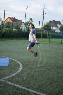 Spor giyim sektöründe genç bir adam sabah spor sahasında spor aleti kullanarak spor yapıyor. Forma olan bağlılığı odaklanma ve enerjiyle eğitim rutinini gerçekleştiriyor.
