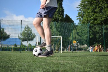 Spor giyimli genç bir adam sabah futbol sahasında antrenman yapıyor. Spor için adanmışlık ve tutku, sabah egzersizinin özü ve açık havada pratik.