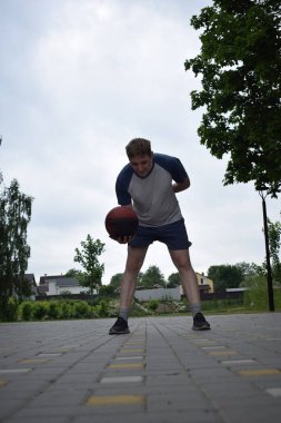 Spor giyimli genç bir adam basketbol oynuyor, sabah spor salonunda antrenman yapıyor. Spor için adanmışlık ve tutku, sabah egzersizinin özü ve açık havada pratik.