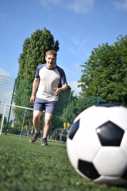 Spor giyimli genç bir adam sabah futbol sahasında antrenman yapıyor. Spor için adanmışlık ve tutku, sabah egzersizinin özü ve açık havada pratik.