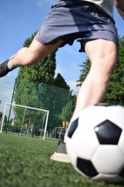 Spor giyimli genç bir adam sabah futbol sahasında antrenman yapıyor. Spor için adanmışlık ve tutku, sabah egzersizinin özü ve açık havada pratik.