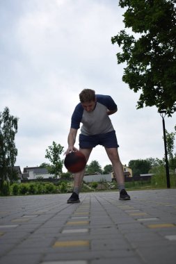 Spor giyimli genç bir adam basketbol oynuyor, sabah spor salonunda antrenman yapıyor. Spor için adanmışlık ve tutku, sabah egzersizinin özü ve açık havada pratik.