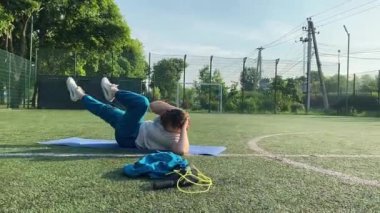Odaklanmış genç bir bayan atlet dinamik bir şekilde ısınma egzersizleri yapıyor ve dışarıda esniyor. Spor giyim sektöründe bedenini düzenli bir rutin içinde fiziksel taleplere özenle hazırlar.
