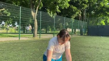 Odaklanmış genç bir bayan atlet dinamik bir şekilde ısınma egzersizleri yapıyor ve dışarıda esniyor. Spor giyim sektöründe bedenini düzenli bir rutin içinde fiziksel taleplere özenle hazırlar.