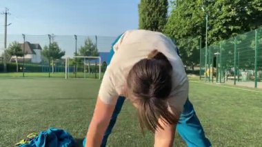 Odaklanmış genç bir bayan atlet dinamik bir şekilde ısınma egzersizleri yapıyor ve dışarıda esniyor. Spor giyim sektöründe bedenini düzenli bir rutin içinde fiziksel taleplere özenle hazırlar.