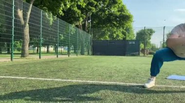 Odaklanmış genç bir bayan atlet dinamik bir şekilde ısınma egzersizleri yapıyor ve dışarıda esniyor. Spor giyim sektöründe bedenini düzenli bir rutin içinde fiziksel taleplere özenle hazırlar.