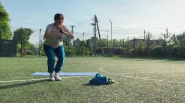 Odaklanmış genç bir bayan atlet dinamik bir şekilde ısınma egzersizleri yapıyor ve dışarıda esniyor. Spor giyim sektöründe bedenini düzenli bir rutin içinde fiziksel taleplere özenle hazırlar.