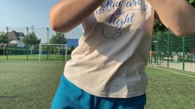 Odaklanmış genç bir bayan atlet dinamik bir şekilde ısınma egzersizleri yapıyor ve dışarıda esniyor. Spor giyim sektöründe bedenini düzenli bir rutin içinde fiziksel taleplere özenle hazırlar.