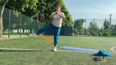 Odaklanmış genç bir bayan atlet dinamik bir şekilde ısınma egzersizleri yapıyor ve dışarıda esniyor. Spor giyim sektöründe bedenini düzenli bir rutin içinde fiziksel taleplere özenle hazırlar.