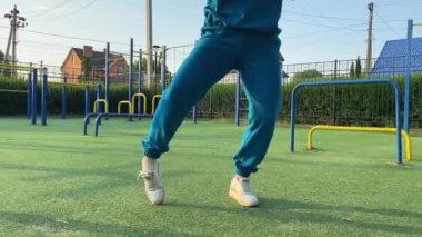 Odaklanmış genç bir bayan atlet dinamik bir şekilde ısınma egzersizleri yapıyor ve dışarıda esniyor. Spor giyim sektöründe bedenini düzenli bir rutin içinde fiziksel taleplere özenle hazırlar.