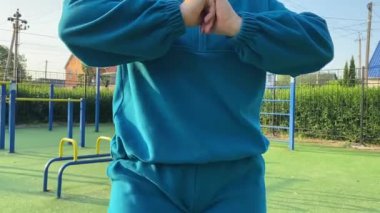 Odaklanmış genç bir bayan atlet dinamik bir şekilde ısınma egzersizleri yapıyor ve dışarıda esniyor. Spor giyim sektöründe bedenini düzenli bir rutin içinde fiziksel taleplere özenle hazırlar.