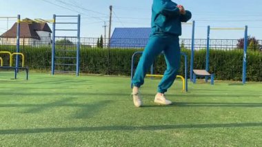 Odaklanmış genç bir bayan atlet dinamik bir şekilde ısınma egzersizleri yapıyor ve dışarıda esniyor. Spor giyim sektöründe bedenini düzenli bir rutin içinde fiziksel taleplere özenle hazırlar.