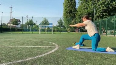 Odaklanmış genç bir bayan atlet dinamik bir şekilde ısınma egzersizleri yapıyor ve dışarıda esniyor. Spor giyim sektöründe bedenini düzenli bir rutin içinde fiziksel taleplere özenle hazırlar.