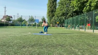 Odaklanmış genç bir bayan atlet dinamik bir şekilde ısınma egzersizleri yapıyor ve dışarıda esniyor. Spor giyim sektöründe bedenini düzenli bir rutin içinde fiziksel taleplere özenle hazırlar.