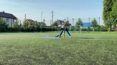 Odaklanmış genç bir bayan atlet dinamik bir şekilde ısınma egzersizleri yapıyor ve dışarıda esniyor. Spor giyim sektöründe bedenini düzenli bir rutin içinde fiziksel taleplere özenle hazırlar.