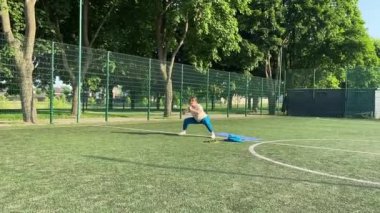 Odaklanmış genç bir bayan atlet dinamik bir şekilde ısınma egzersizleri yapıyor ve dışarıda esniyor. Spor giyim sektöründe bedenini düzenli bir rutin içinde fiziksel taleplere özenle hazırlar.