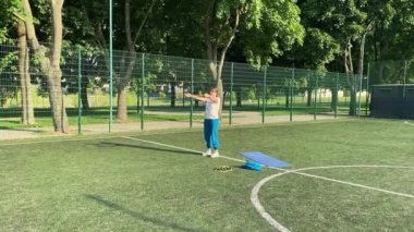 Odaklanmış genç bir bayan atlet dinamik bir şekilde ısınma egzersizleri yapıyor ve dışarıda esniyor. Spor giyim sektöründe bedenini düzenli bir rutin içinde fiziksel taleplere özenle hazırlar.