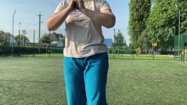 Odaklanmış genç bir bayan atlet dinamik bir şekilde ısınma egzersizleri yapıyor ve dışarıda esniyor. Spor giyim sektöründe bedenini düzenli bir rutin içinde fiziksel taleplere özenle hazırlar.