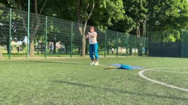 Odaklanmış genç bir bayan atlet dinamik bir şekilde ısınma egzersizleri yapıyor ve dışarıda esniyor. Spor giyim sektöründe bedenini düzenli bir rutin içinde fiziksel taleplere özenle hazırlar.