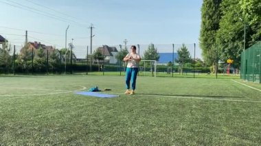 Odaklanmış genç bir bayan atlet dinamik bir şekilde ısınma egzersizleri yapıyor ve dışarıda esniyor. Spor giyim sektöründe bedenini düzenli bir rutin içinde fiziksel taleplere özenle hazırlar.