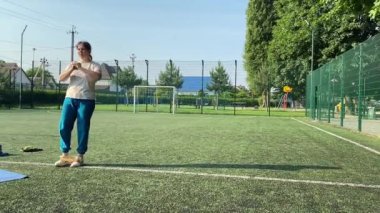 Odaklanmış genç bir bayan atlet dinamik bir şekilde ısınma egzersizleri yapıyor ve dışarıda esniyor. Spor giyim sektöründe bedenini düzenli bir rutin içinde fiziksel taleplere özenle hazırlar.