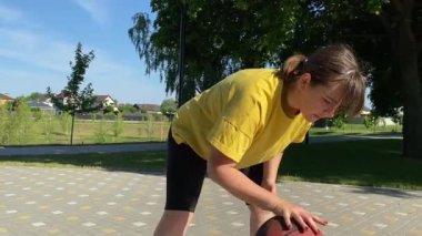 Spor giyim sektöründe genç bir kadın basketbol oynuyor, sabah bir spor sahasında antrenman yapıyor. Spor için adanmışlık ve tutku, sabah egzersizinin özü ve açık havada pratik.