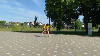Spor giyim sektöründe genç bir kadın basketbol oynuyor, sabah bir spor sahasında antrenman yapıyor. Spor için adanmışlık ve tutku, sabah egzersizinin özü ve açık havada pratik.