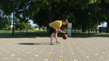 Spor giyim sektöründe genç bir kadın basketbol oynuyor, sabah bir spor sahasında antrenman yapıyor. Spor için adanmışlık ve tutku, sabah egzersizinin özü ve açık havada pratik.