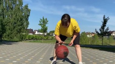 Spor giyim sektöründe genç bir kadın basketbol oynuyor, sabah bir spor sahasında antrenman yapıyor. Spor için adanmışlık ve tutku, sabah egzersizinin özü ve açık havada pratik.