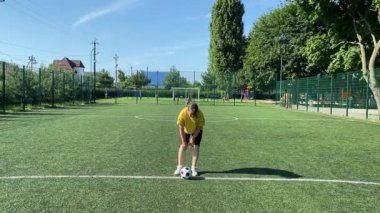 Spor giyimli genç bir kadın sabah futbol sahasında antrenman yapıyor. Spor için adanmışlık ve tutku, sabah egzersizinin özü ve açık havada pratik.