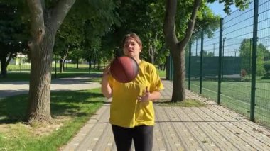 Spor giyimli genç bir kadın basketbol oynayacak, sabah bir spor sahasında antrenman yapacak. Spor için adanmışlık ve tutku, sabah egzersizinin özü ve açık havada pratik.